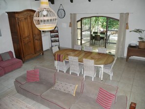 Un salon comprenant une table à manger, des chaises en osier, un ensemble de canapés, un meuble en bois et une grande fenêtre.