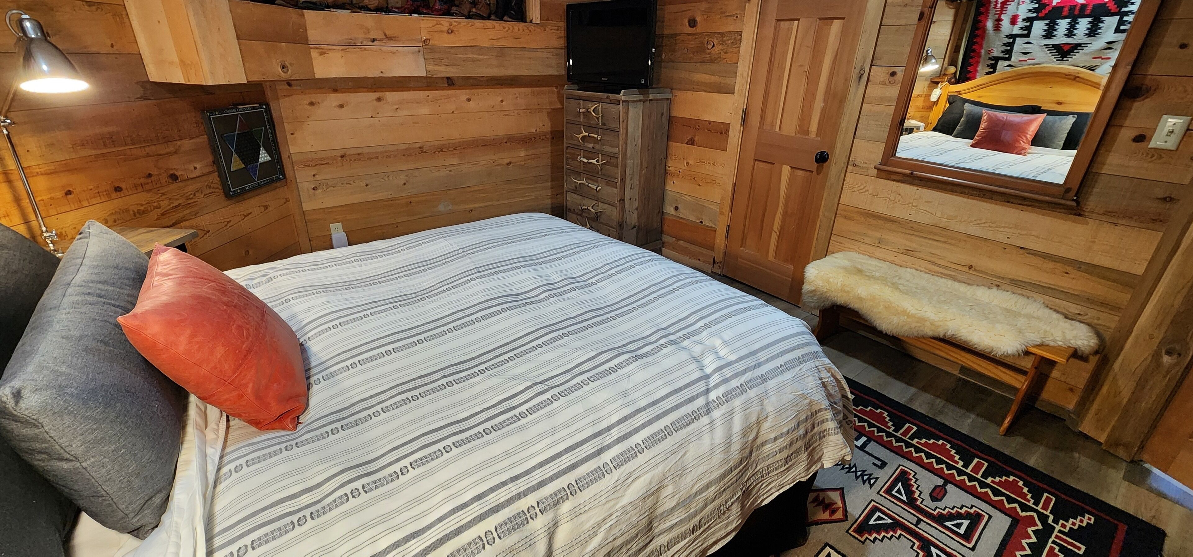 A cozy wooden room with a bed, a bench, a dresser, and a TV.