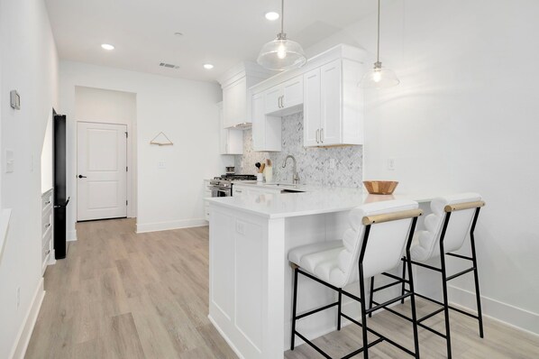 A modern kitchen with white cabinetry, a marble backsplash, and a central island with bar stools. - The Brick House in Rogers (Rogers)