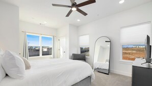 Ein Schlafzimmer mit einem großen Bett, einem Deckenventilator, einem Fernseher und Blick ins Freie.
