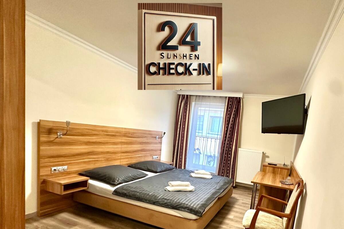 Habitación de hotel con cama, escritorio, televisión y ventana con cortinas.