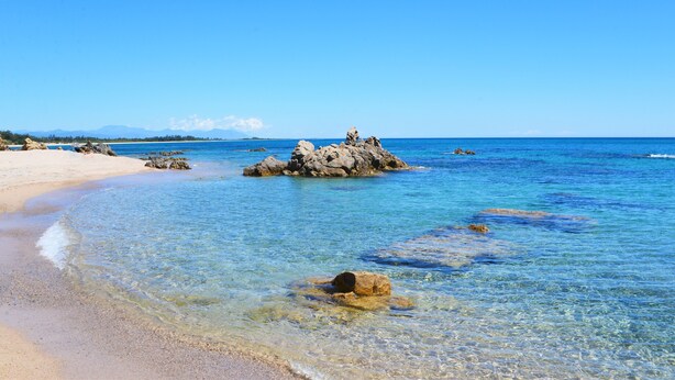 A beach with clear water, rocks, and a sandy shore.