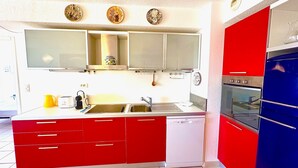 A kitchen with red cabinets, a white dishwasher, a blue oven, and a stainless steel sink.