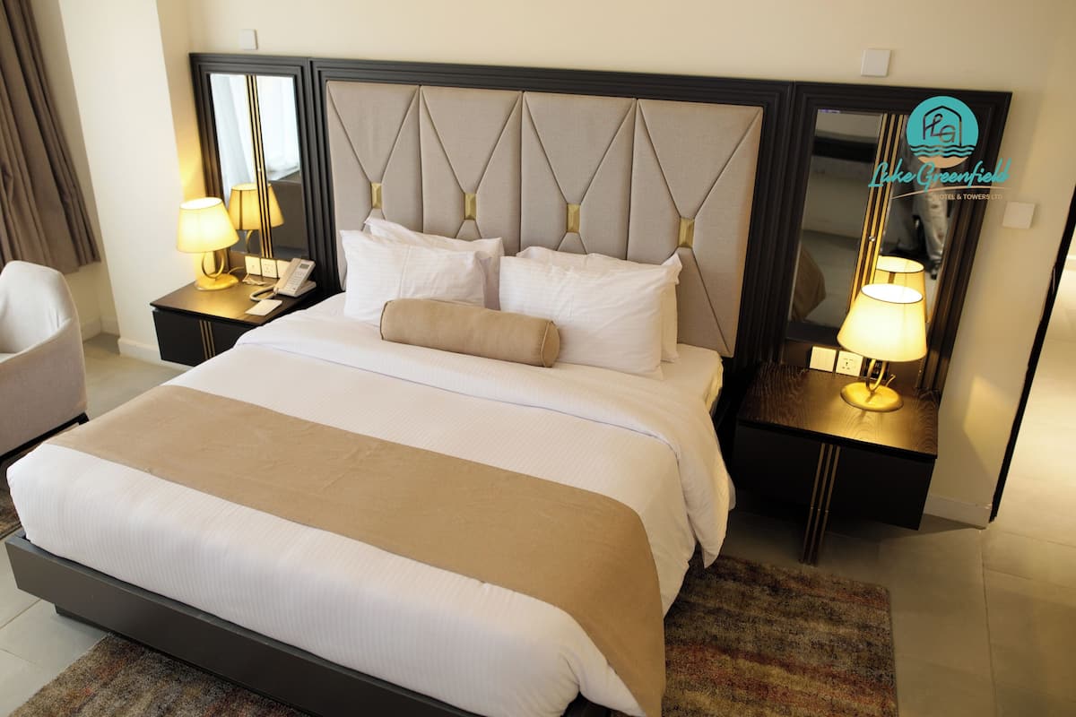 Une chambre d’hôtel avec un grand lit, une chaise, une table de chevet avec une lampe et un miroir.