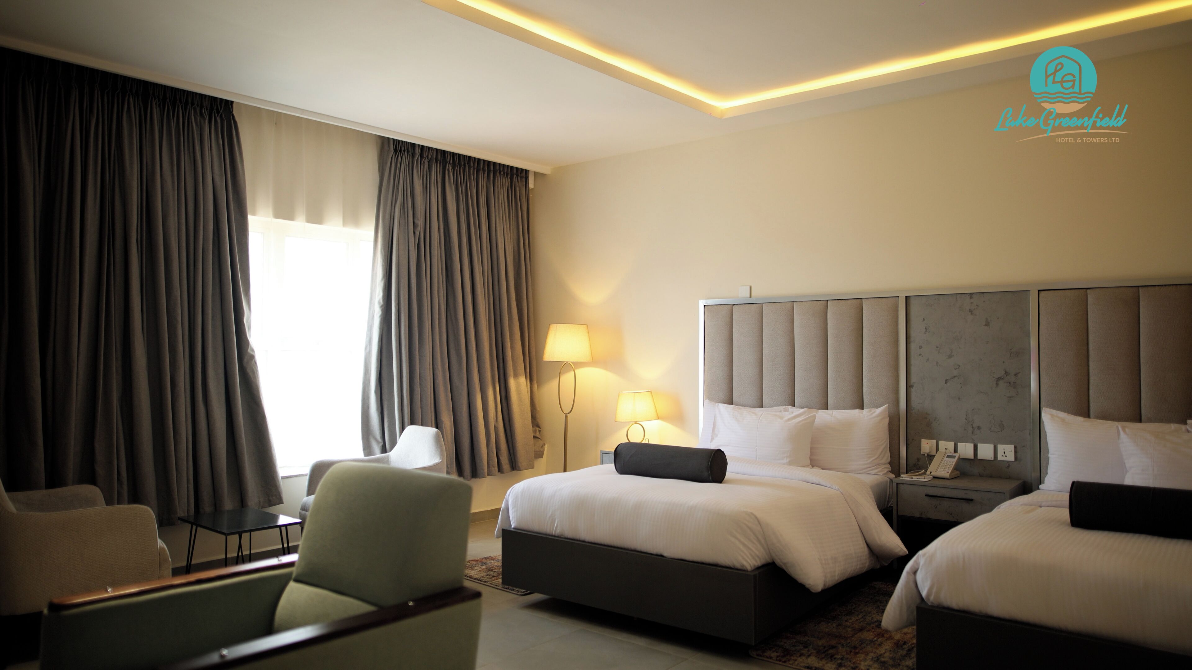 A hotel room with two beds, a desk, a chair, and a lamp.