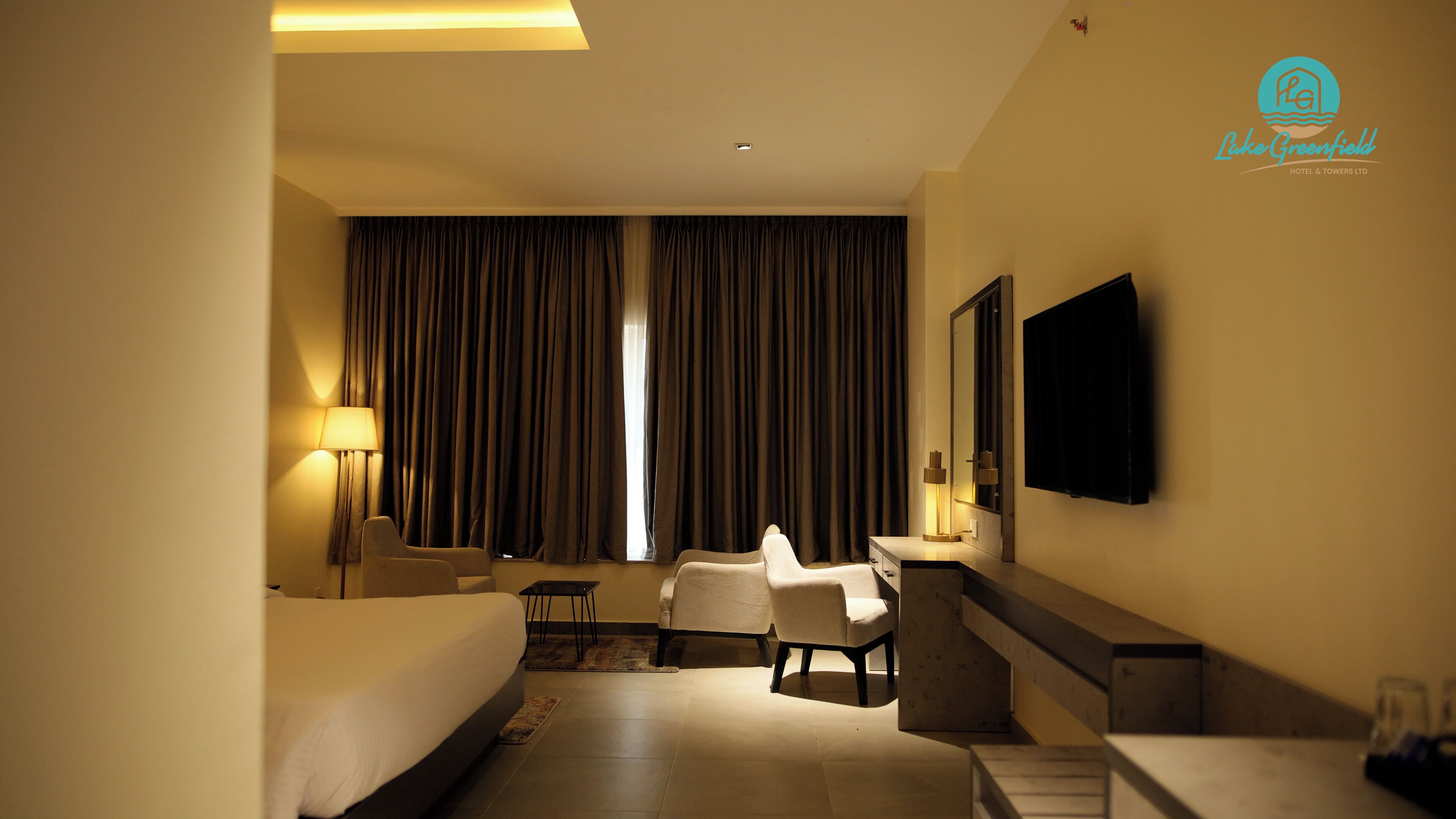 A hotel room with a bed, two armchairs, a desk, a TV, and a window with curtains.