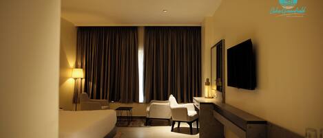 A hotel room with a bed, two armchairs, a desk, a TV, and a window with curtains.