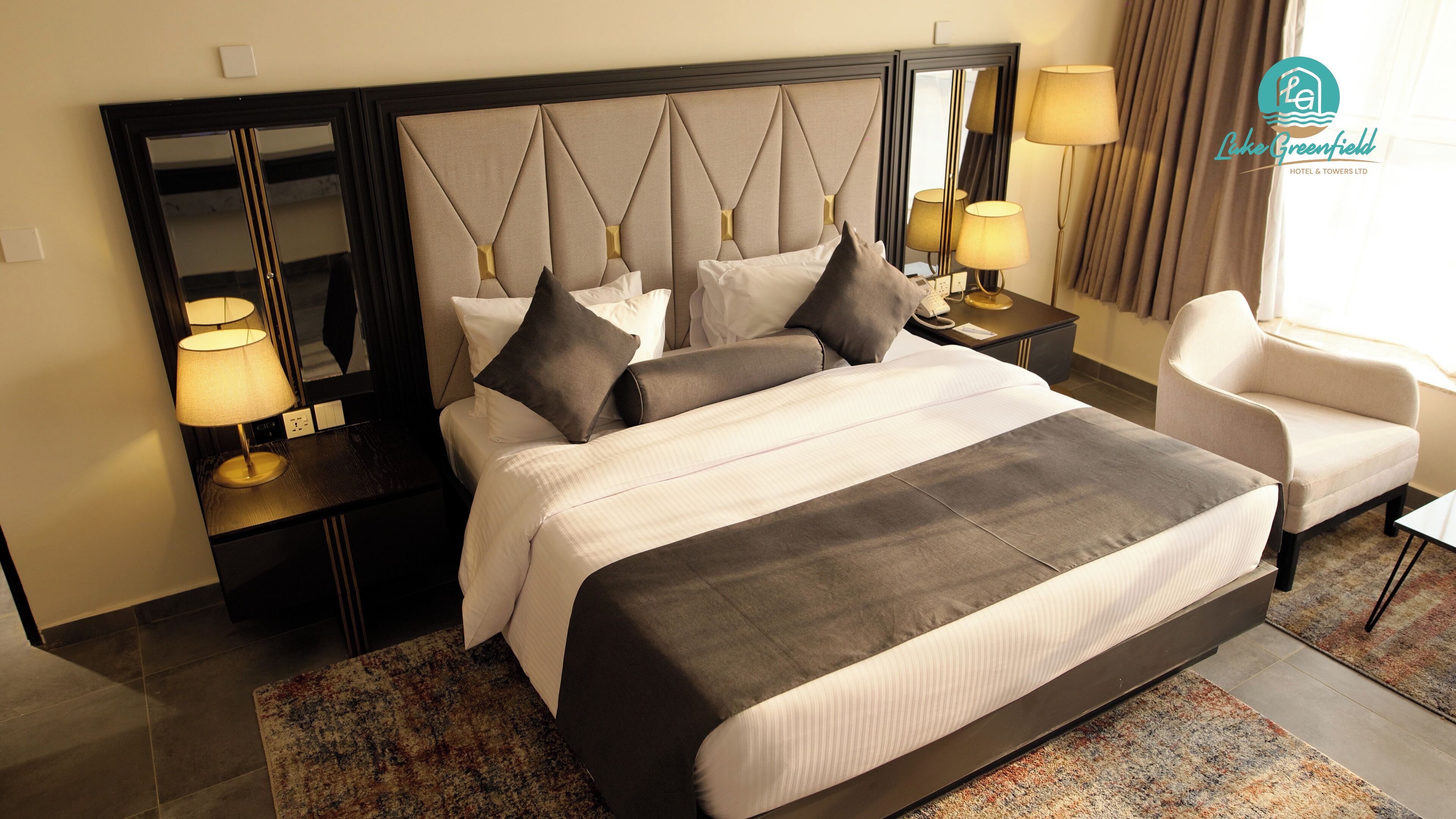 Quarto de hotel com uma cama grande, duas mesas de cabeceira com luminárias, uma cadeira e um espelho grande sobre a cama.