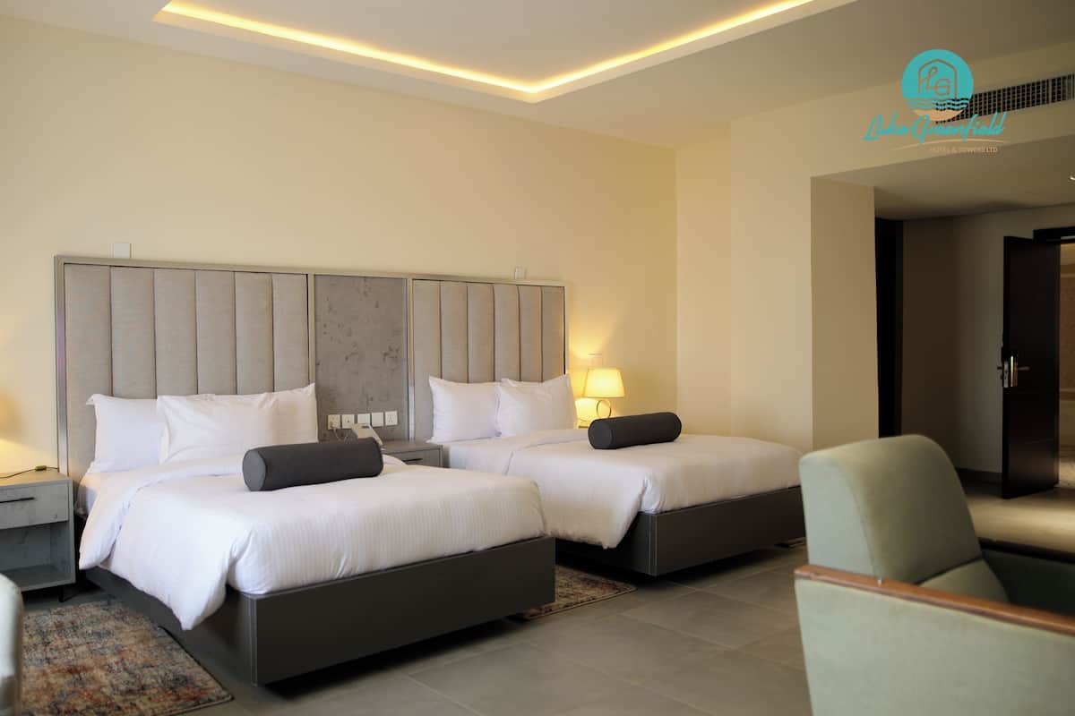 Une chambre d’hôtel avec deux lits, deux tables de chevet, des lampes, une chaise et un grand miroir.