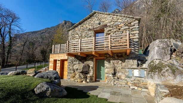 A stone cabin with a wooden balcony, surrounded by rocks and grass, set against a mountainous backdrop. - Peace in the nature close to Palazzo Vertemate, Madesimo and Engadina. (Lombardia)