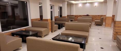 A modern lounge area with sofas and tables, a large window, and a brick accent wall.