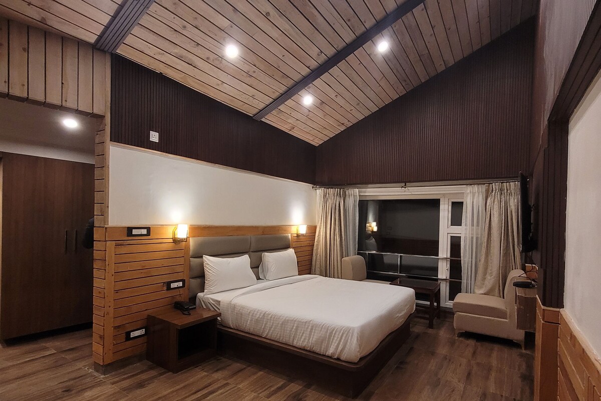 A spacious bedroom with a large bed, wooden paneling on the walls, a wooden floor, and a window with curtains.