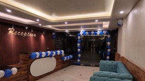 A reception area with a wooden reception desk, blue and white balloons, and a teal sofa. - Faagu Peaks (Theog)
