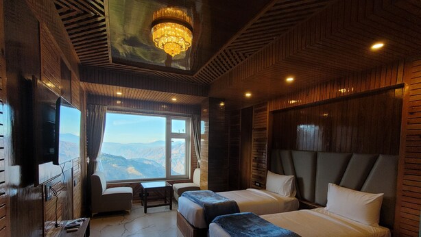 A room with two beds, a desk, a chair, and a large window offering a mountain view. - Faagu Peaks (Theog)