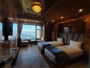 Ein Zimmer mit zwei Betten, einem Schreibtisch, einem Stuhl und einem großen Fenster mit Blick auf die Berge.