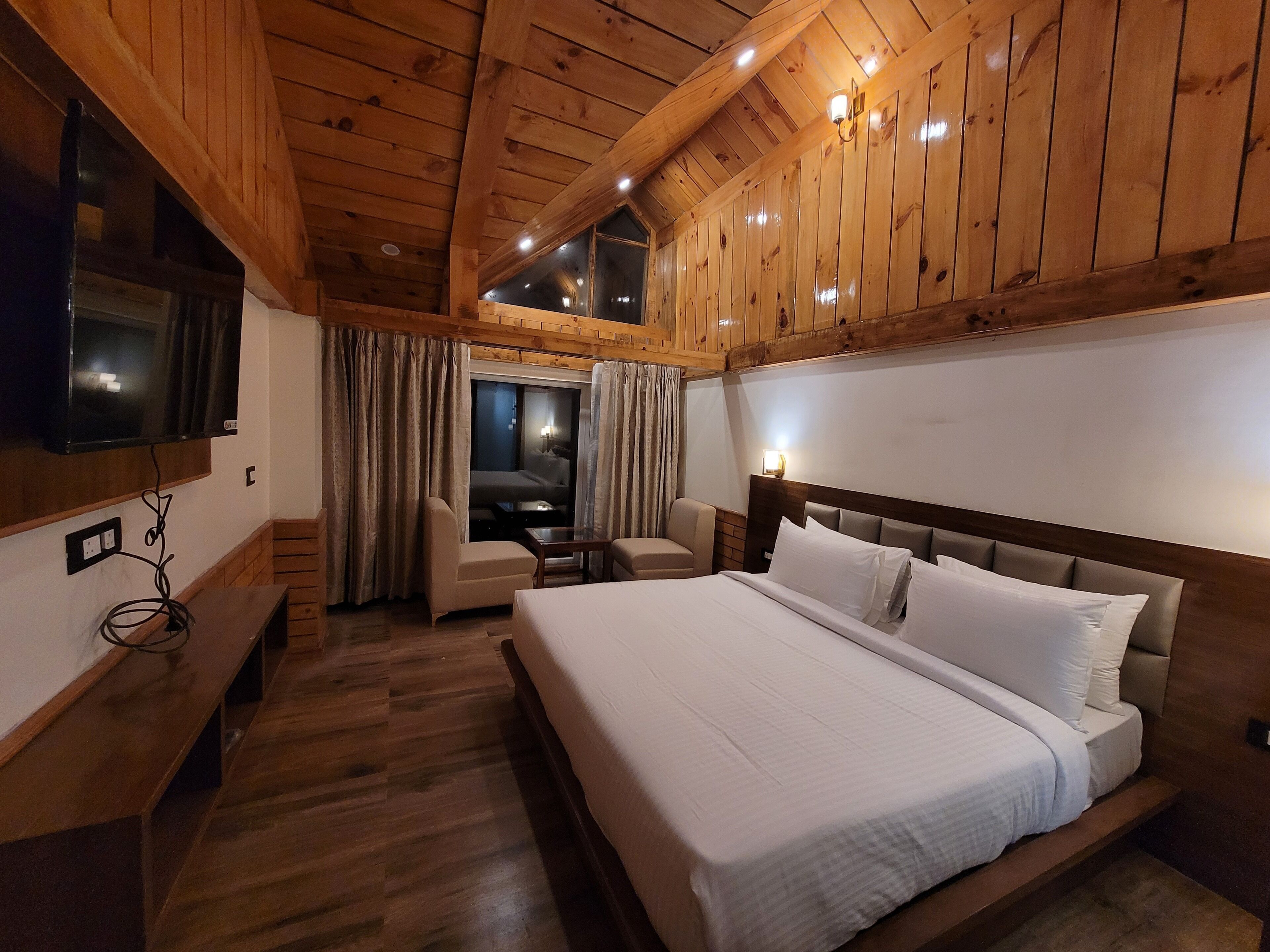 A wooden-paneled room with a bed, a TV mounted on the wall, and a desk with a chair.