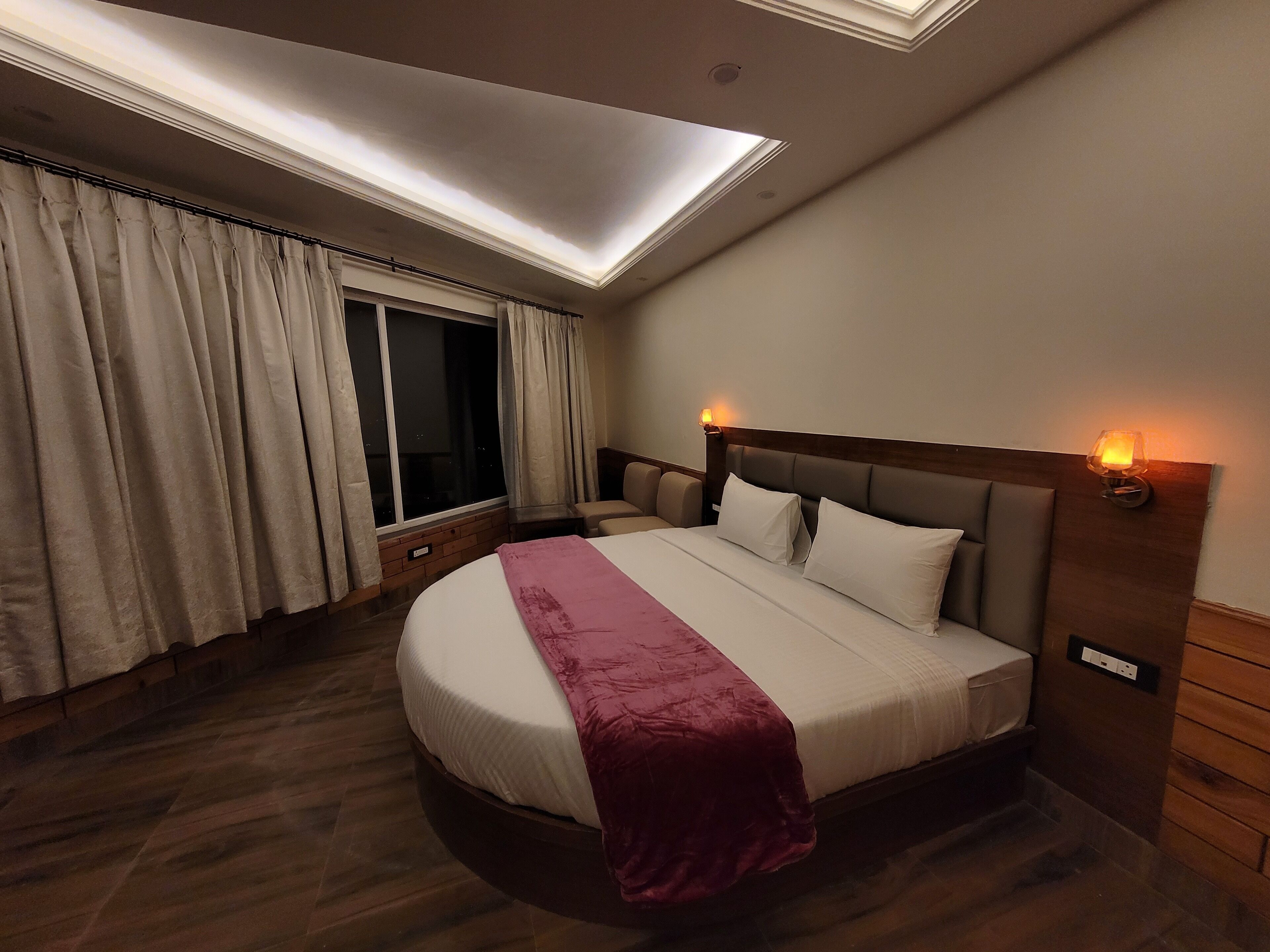 Une chambre d’hôtel avec un grand lit, une lucarne, une fenêtre avec des rideaux et une table de chevet avec une lampe.