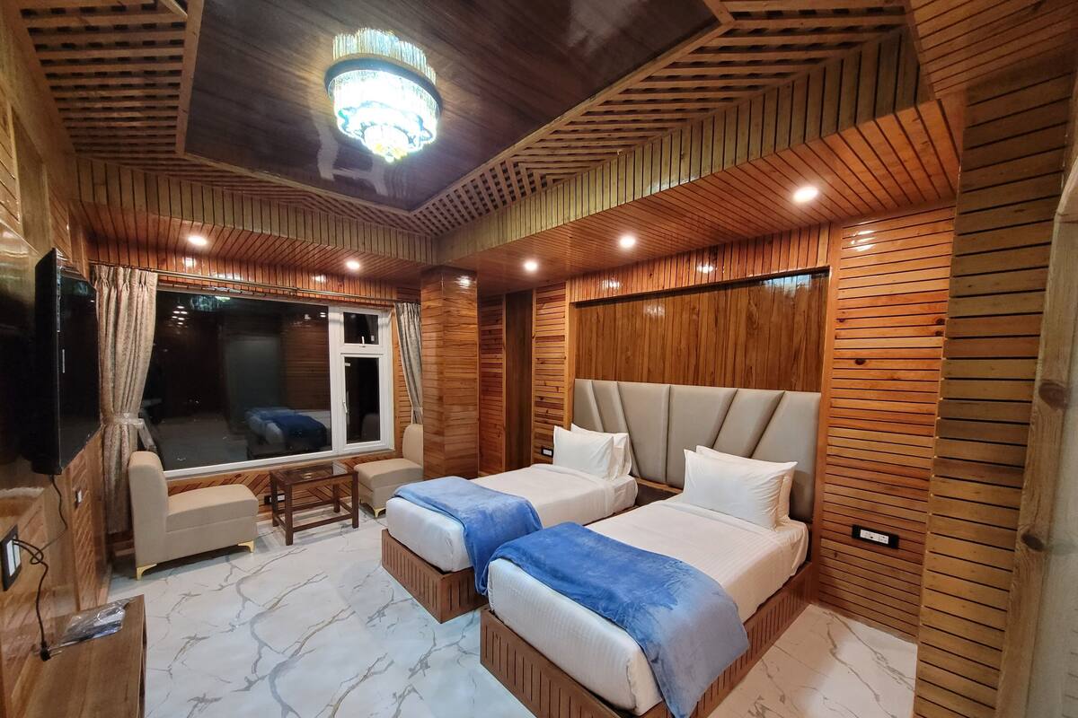 Una habitación con dos camas, televisión, ventana con cortinas y candelabro.