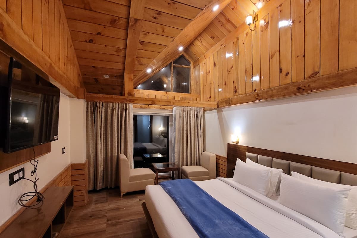 Habitación con paneles de madera, una cama, un televisor, un escritorio y vistas a un balcón.