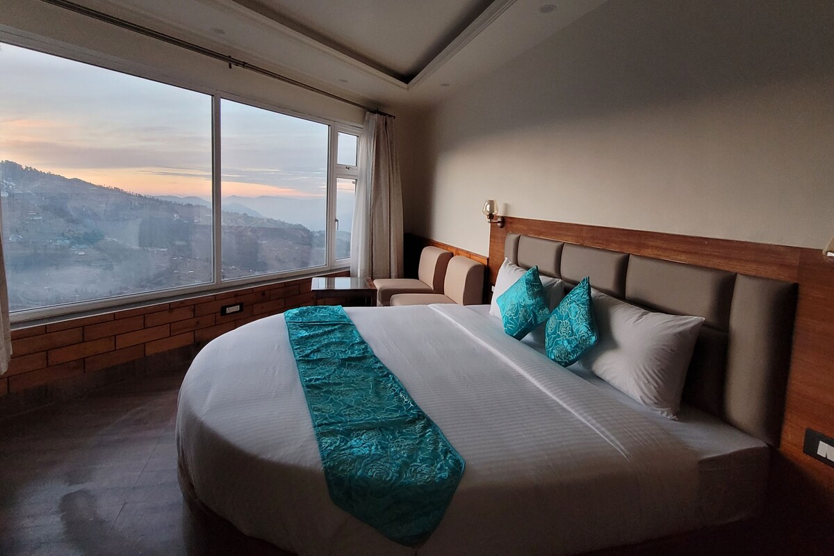 A hotel room with a large bed, a view of a mountainous landscape, and a wooden headboard.
