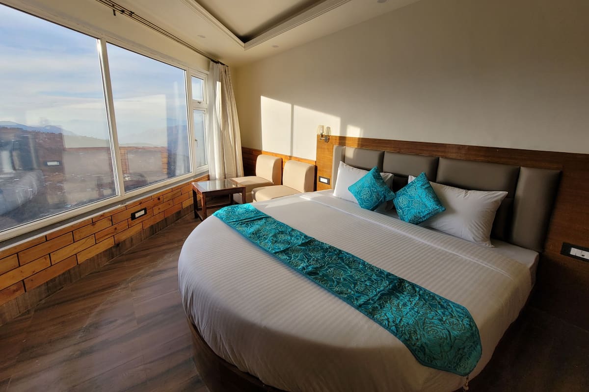 Habitación de hotel con una cama grande, cabecera de madera, mesita de noche y vistas al exterior a través de un ventanal amplio.