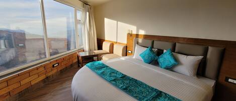 A hotel room with a large bed, a wooden headboard, a nightstand, a bedside table, and a window with curtains.