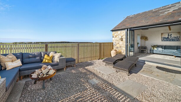 An outdoor patio with a stone wall, a sofa set, and a fire pit.