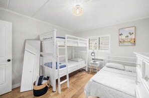 A room with bunk beds, a bedside table with a lamp, a framed picture on the wall, and a door.