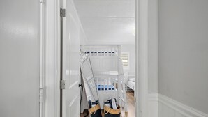 Habitación blanca con una cuna, una puerta y suelo de madera.