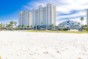 A beachfront hotel with multiple high-rise buildings, a sandy beach, and a parking area with cars.