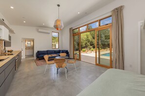 A modern kitchen with a dining area, a sofa, and a view of a swimming pool.