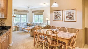 A cozy living room with a sofa, a dining table with chairs, and a kitchen area with wooden cabinets. - Beautiful Deluxe 2 Bedroom Condo in Smugglers Notch Resort (Jeffersonville)