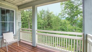 A wooden deck with a white railing, a bench, and a view of a forested area. - Beautiful Deluxe 2 Bedroom Condo in Smugglers Notch Resort (Jeffersonville)
