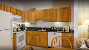 A kitchen with wooden cabinets, a white refrigerator, a microwave, a stove, a dishwasher, and a chair. - Beautiful Deluxe 2 Bedroom Condo in Smugglers Notch Resort (Jeffersonville)