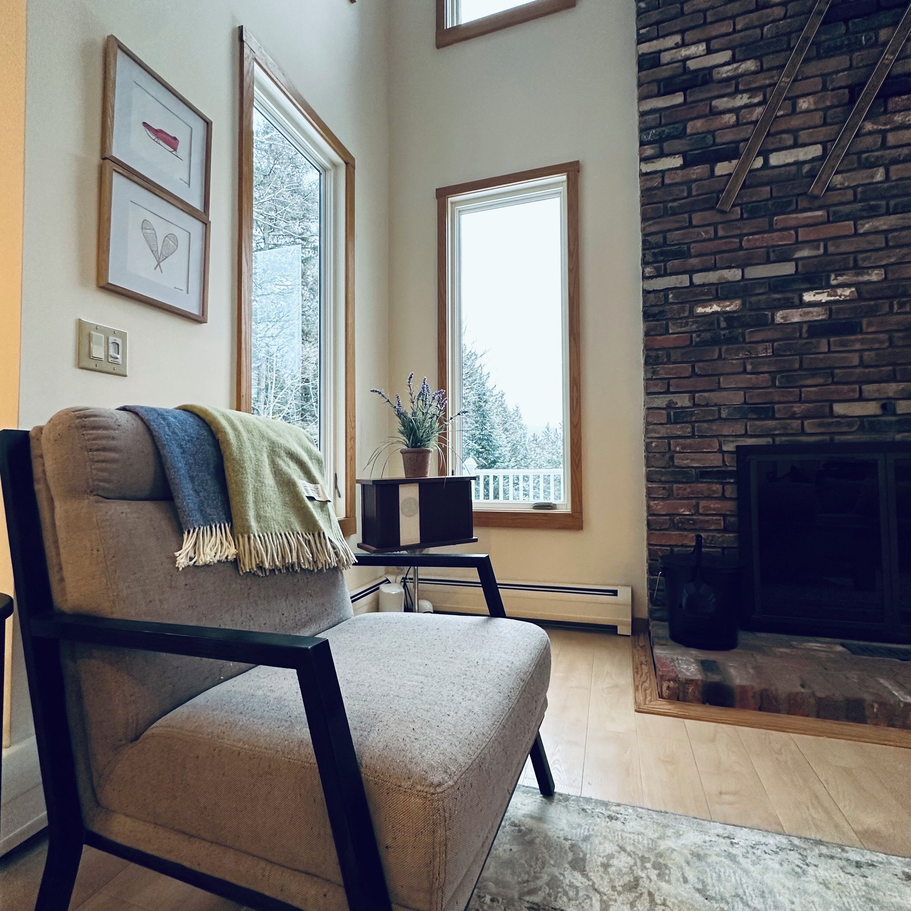 A living room with a fireplace, a large window, and a chair with a throw blanket.