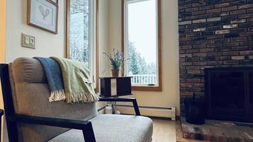 A living room with a fireplace, a large window, and a chair with a throw blanket.