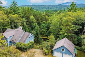 A residential area with two blue houses surrounded by dense forest and a mountain in the background. - Relax & Recover Mountain Retreat - Hot Tub + Sauna + Home Gym (Winhall)