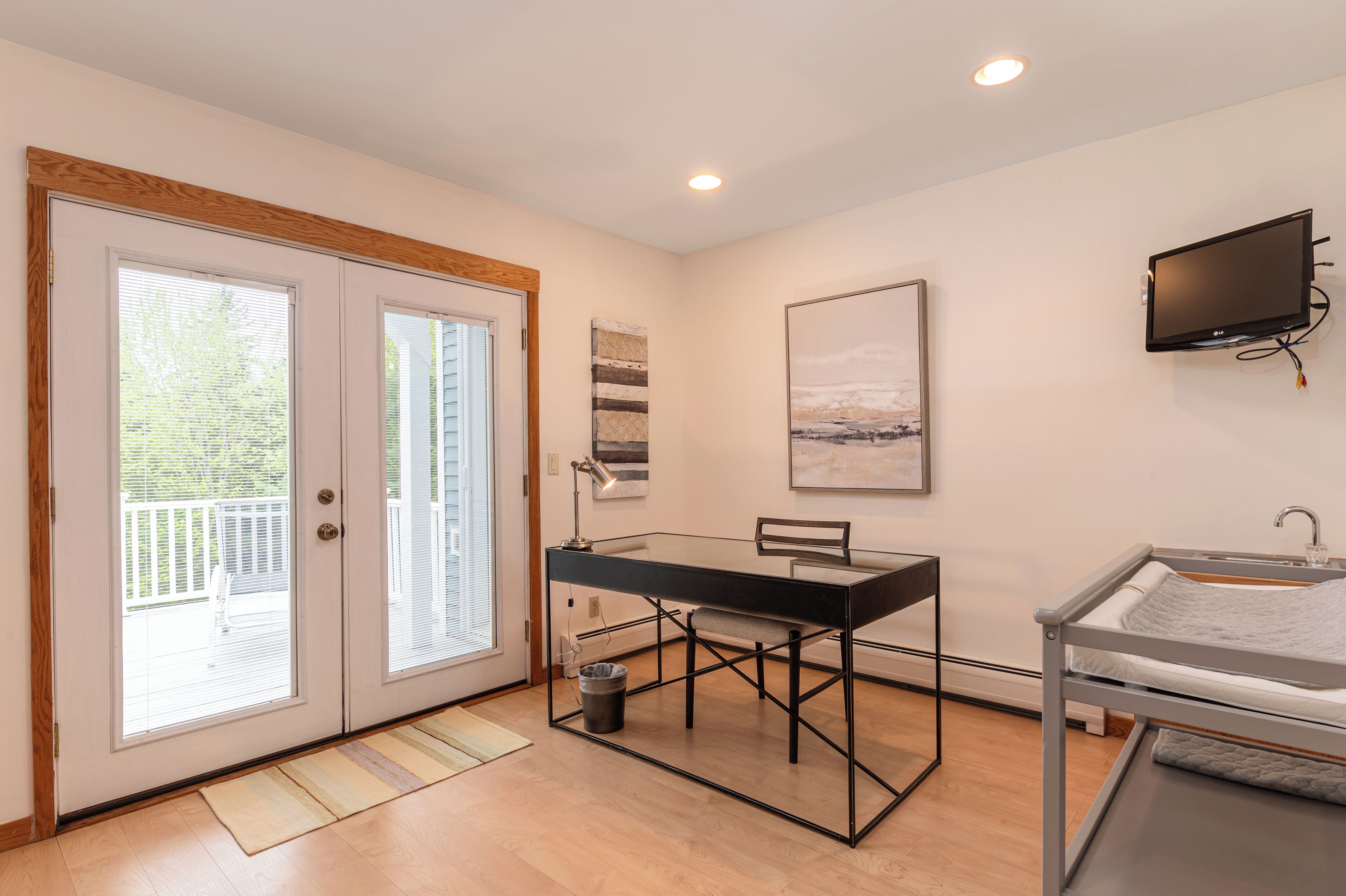 A modern room with a glass desk, a bed, a TV, and a balcony door.