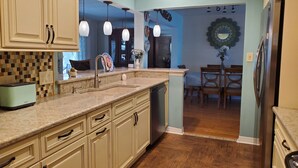 A kitchen with beige cabinets, a granite countertop, a sink, and a dishwasher. There is a dining area with a table and chairs visible through an open doorway. - Butterfly House, close to beaches, restaurants, live entertainment & shopping (Sarasota)