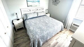 Un dormitorio con cama, mesitas de noche, una obra de arte en la pared y un adorno colgante.