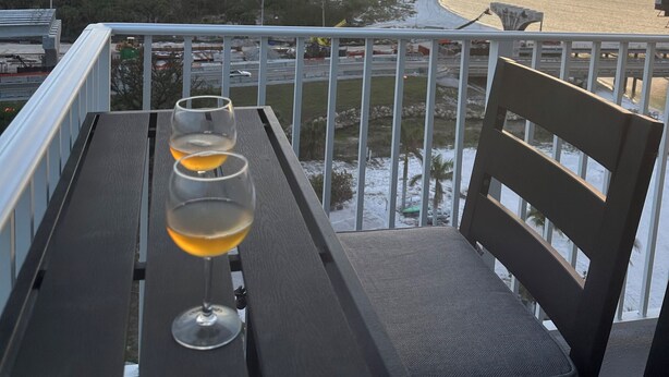 Un balcón con una mesa y dos copas de vino, con vistas al agua y una costa lejana.