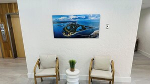 Un vestíbulo con dos sillas de madera, una pequeña mesa blanca con una planta y un cuadro grande de un paisaje costero en la pared.