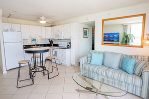 A modern kitchen with white cabinets, a central island with stools, a dining table, and a large mirror above a sofa with striped cushions.