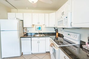 Una cocina con armarios blancos, un refrigerador, un microondas, una estufa y un lavamanos.