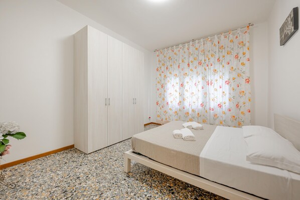 Une chambre à coucher avec un lit, une armoire, un rideau à motifs floraux et une plante.
