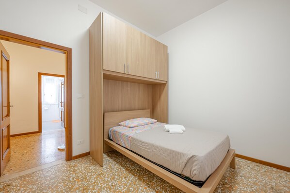 A bedroom with a bed, wooden wardrobe, and a hallway leading to another room.