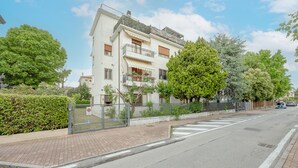 Ein Wohngebäude mit geschlossenem Eingangsbereich, einem gepflasterten Bürgersteig und einer freien Straße.