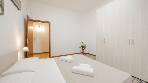 Ein Hotelzimmer mit Bett, Schrank, kleiner Pflanze und Lampe.