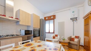 Eine kompakte Küche mit Mikrowelle, Herd, Backofen und Kühlschrank. Ein Esstisch mit Sonnenblumen Tischdecke und eine kleine Sitzecke mit Sofa und Stühlen.