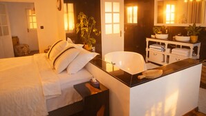 Een moderne slaapkamer met een groot bed, nachtkastje en een kleine badkamer met wastafel en spiegel.